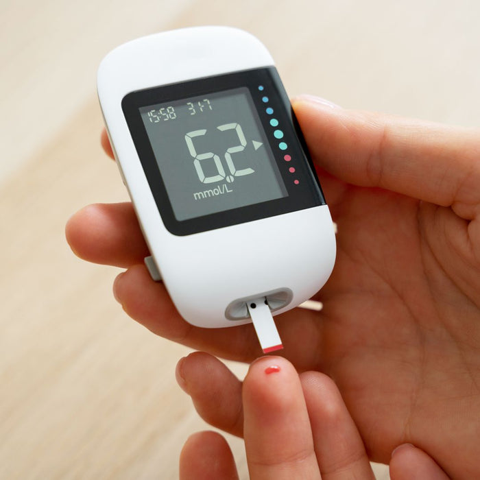 Person holding a digital blood glucose meter with a small drop of blood on the tip.