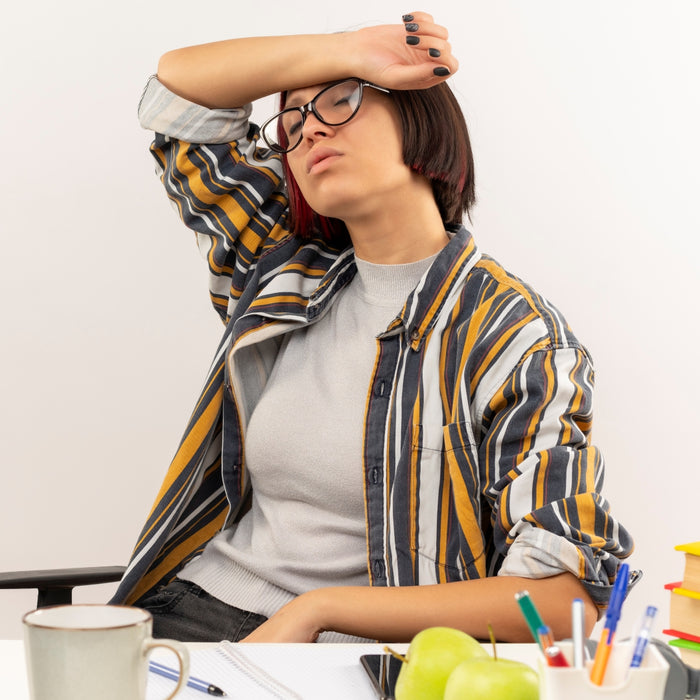 Woman sitting at a desk with a cup, apples, and stationery, appearing stressed.