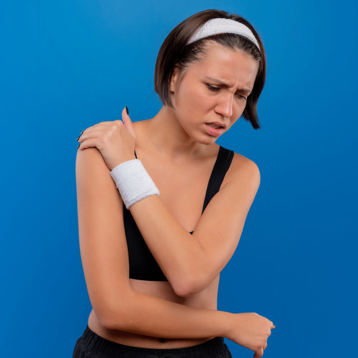 Woman with a sports bra and headband holding her shoulder against a blue background