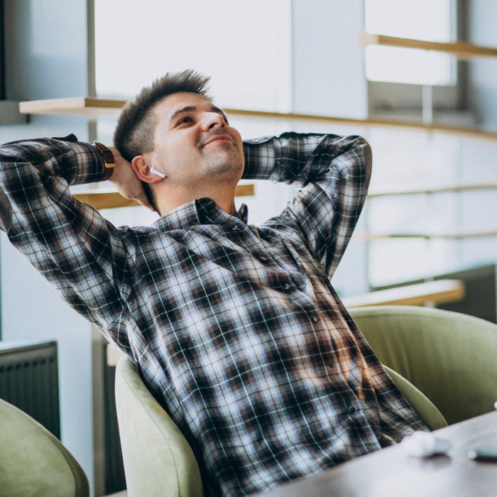 Man in a plaid shirt sitting in a modern office with his hands behind his head.
