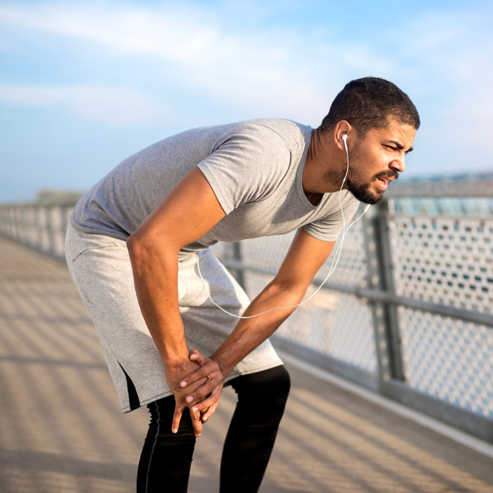 Man stretching outdoors on a bridge with headphones in, wearing a gray t-shirt and black pants.