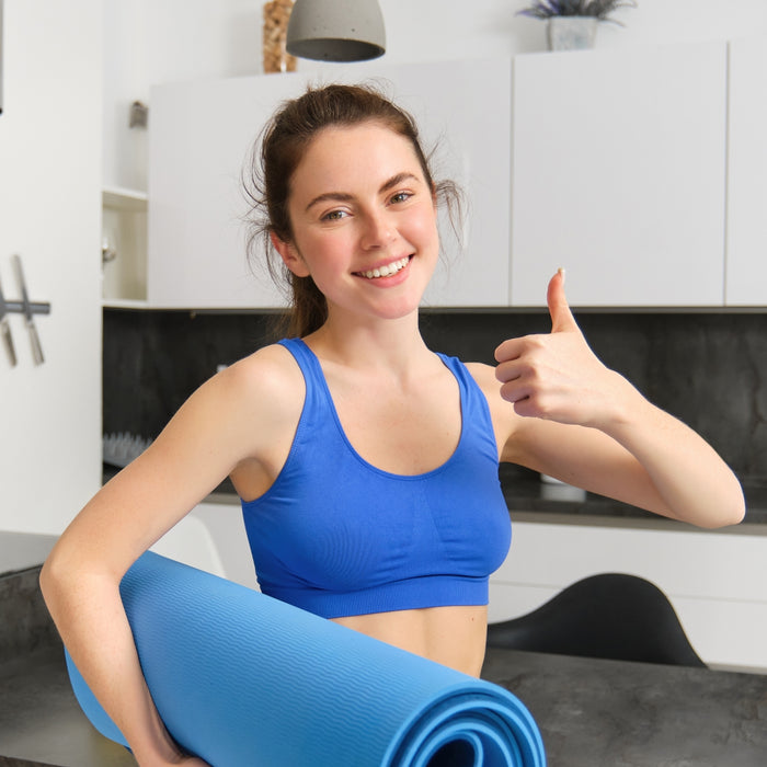 Woman in blue sports bra holding a blue yoga mat in a kitchen