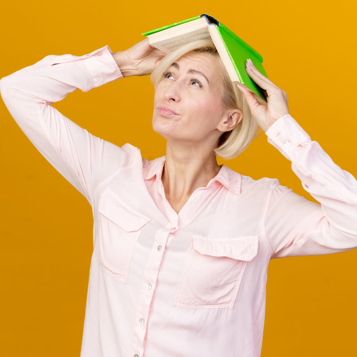 Woman holding a green book on her head against an orange background