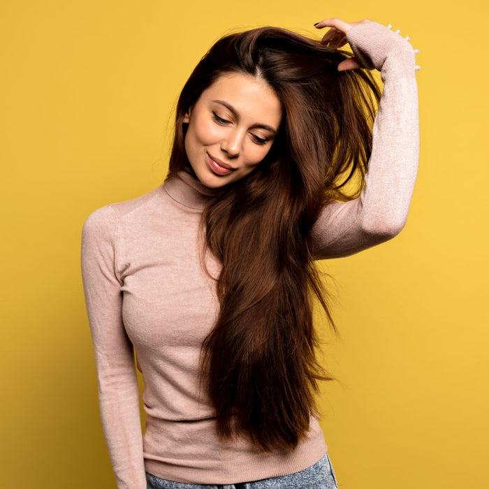 Woman with long brown hair wearing a light pink turtleneck against a yellow background