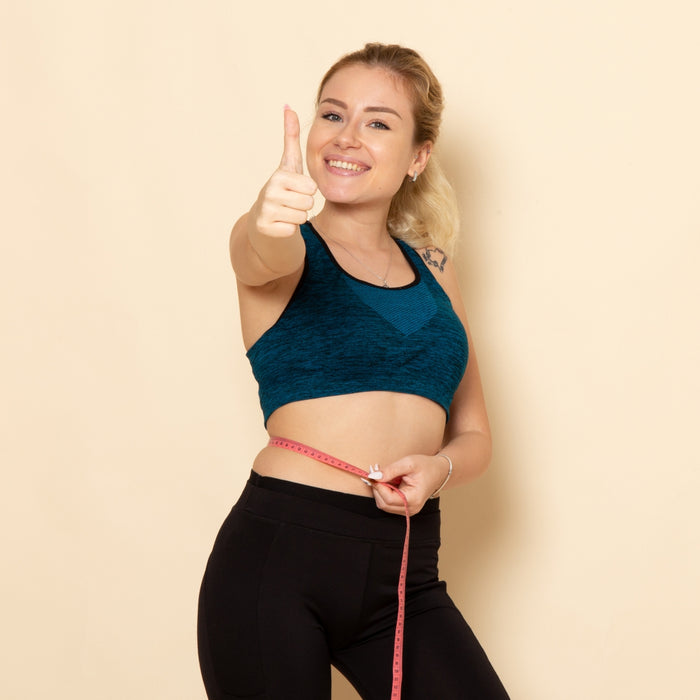 Woman in athletic wear giving a thumbs-up with a measuring tape on a beige background