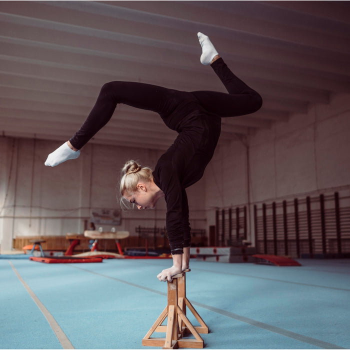Person performing a handstand on a balance beam in a gymnasium.