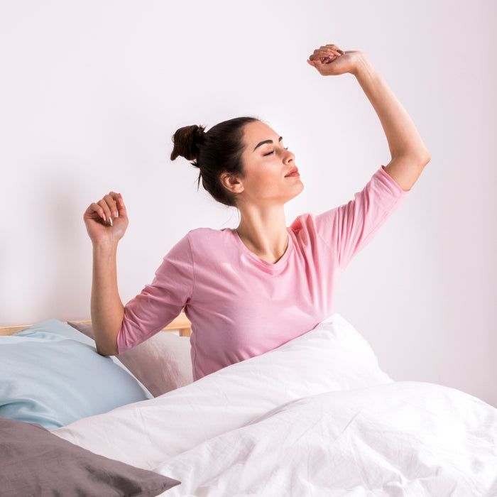 Woman in pink shirt waking up in bed with white bedding