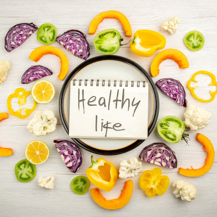 Colorful vegetables arranged around a notebook with 'Healthy Life' text on a light wooden background.