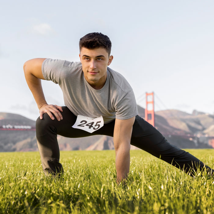 Man in athletic gear with a number on his shirt, stretching outdoors with the Golden Gate Bridge in the background.