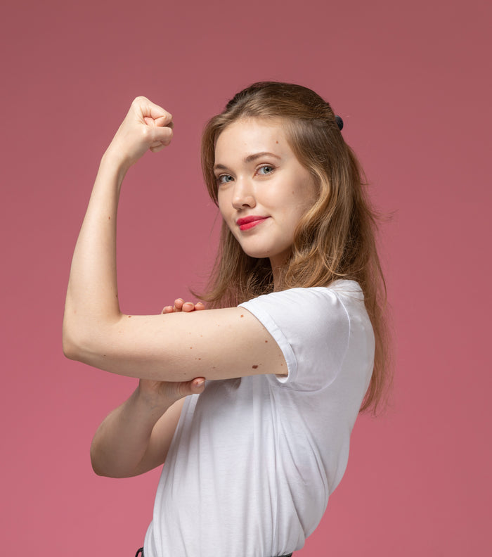 Woman flexing her arm muscles against a pink background