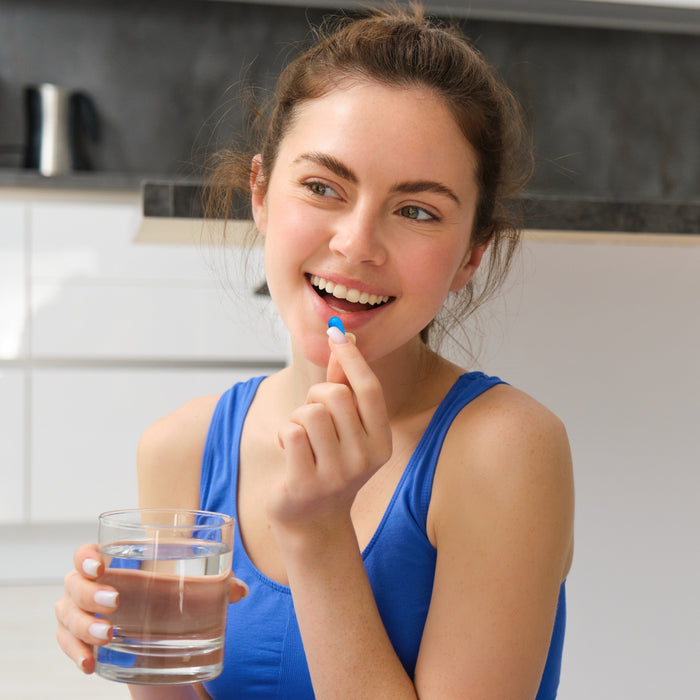 Woman in a kitchen holding a glass of water and holding gutsyral capsules