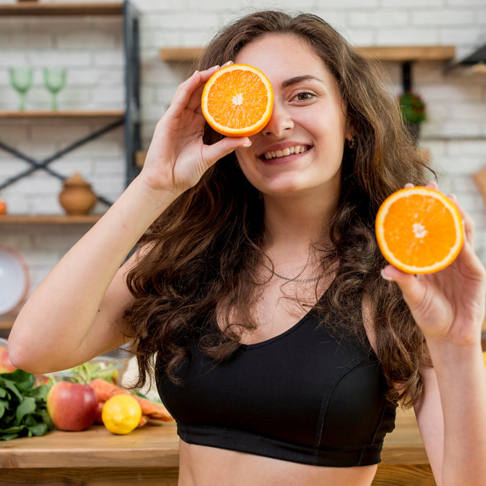Woman holding orange slices in front of her eyes in a kitchen setting
